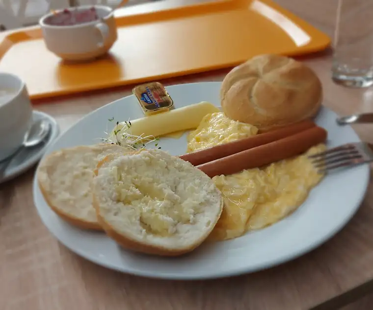 Śniadanie: jajecznica, parówki, bułki i masło na talerzu